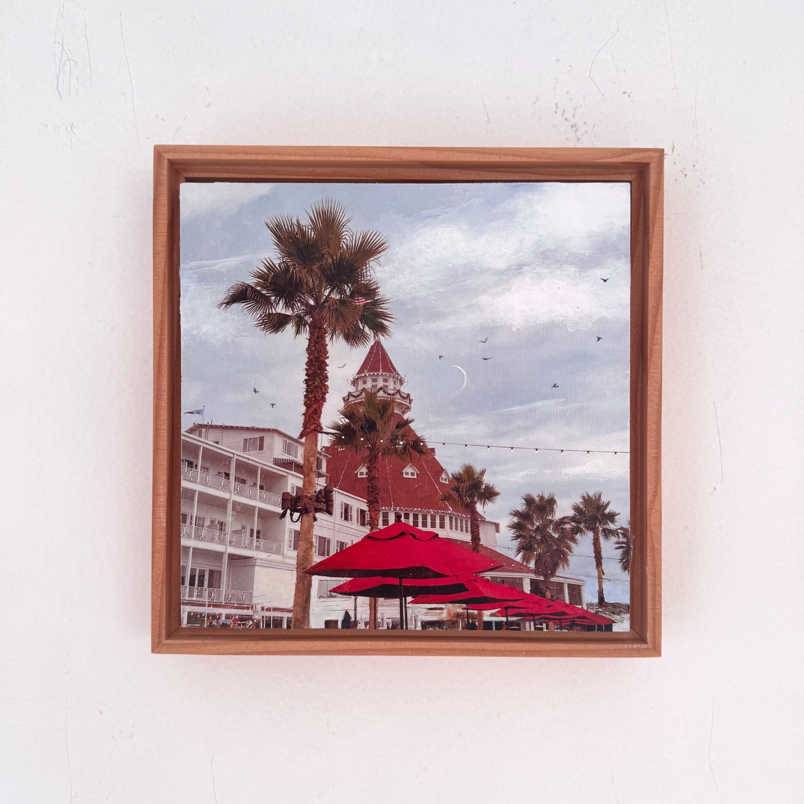 Framed artwork of the hotel del coronado-  with palm trees and a red umbrellas