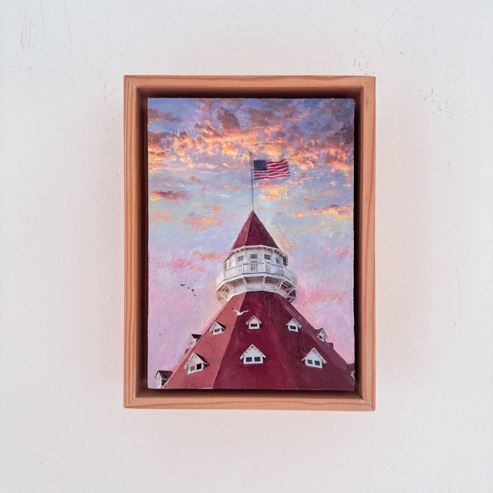 framed artwork of the hotel del coronado with a flag and pink and purple sunset
